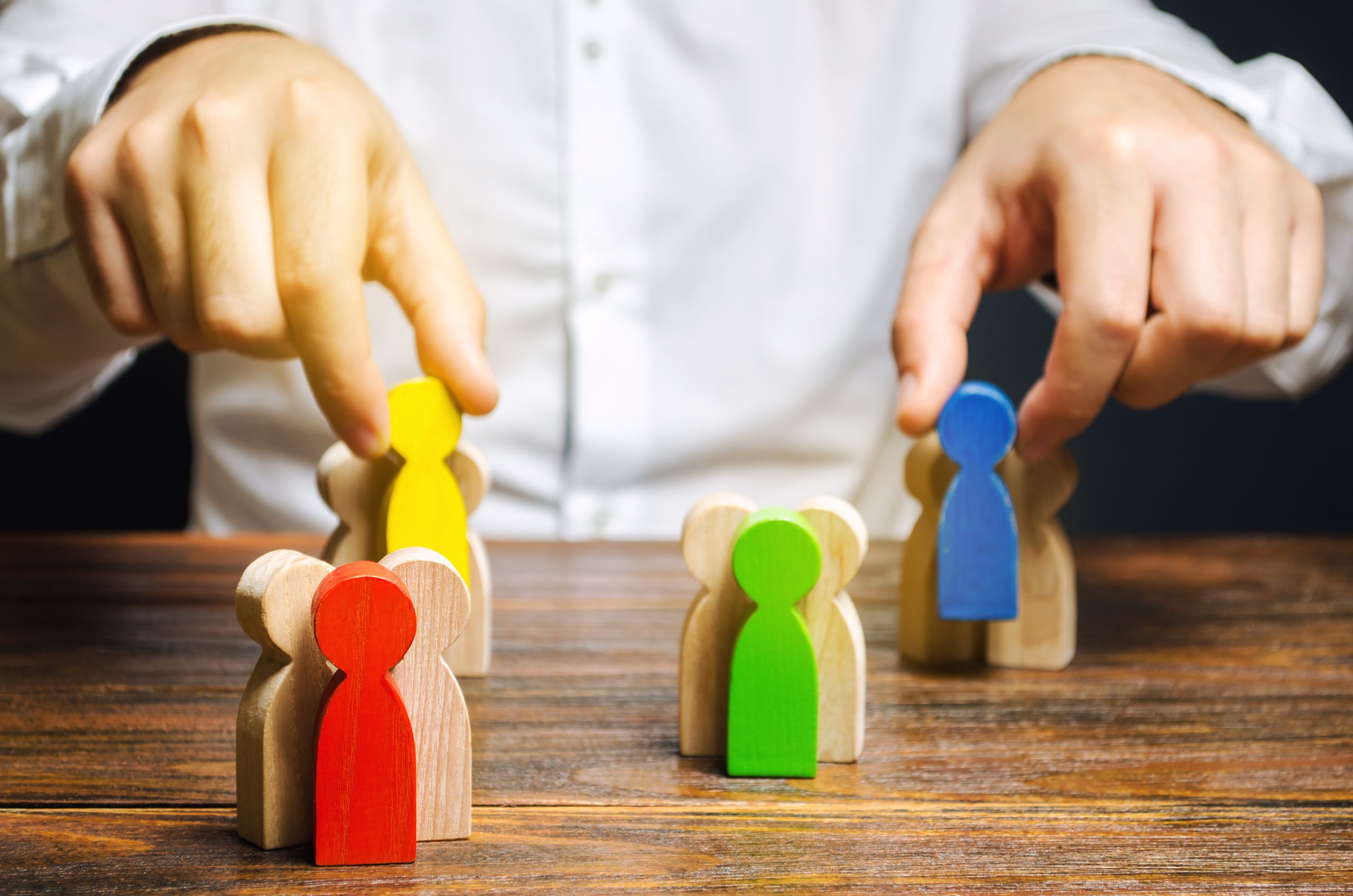 Hands selecting colored wooden figures, representing target population and endpoints validation in clinical trials.